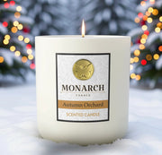 Monarch Candle labeled “Autumn Orchard” glowing gently in a white luxury glass vessel against a warm festive holiday background.