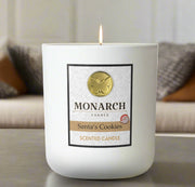 
Monarch Candle labeled “Santa's Cookies” glowing gently in a white luxury glass vessel against a warm indoor background.
