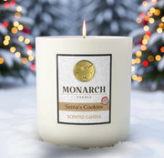 Monarch Candle labeled “Santa's Cookies” glowing gently in a white luxury glass vessel against a warm festive holiday background.