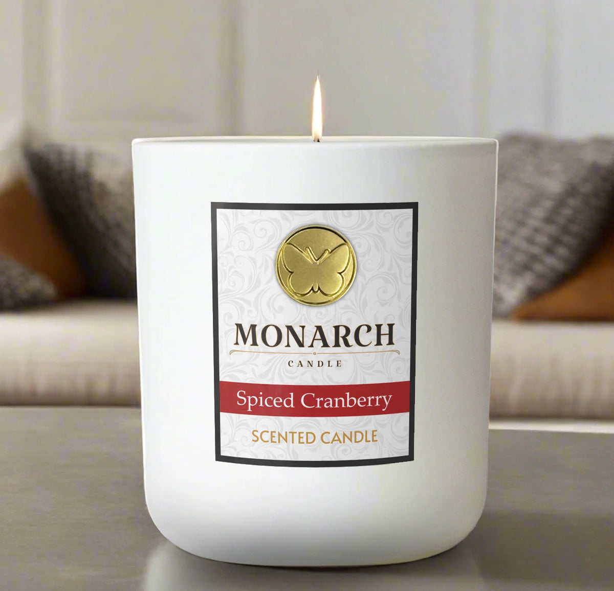 Monarch Candle labeled “Spiced Cranberry” glowing gently in a white luxury glass vessel against a warm indoor background.