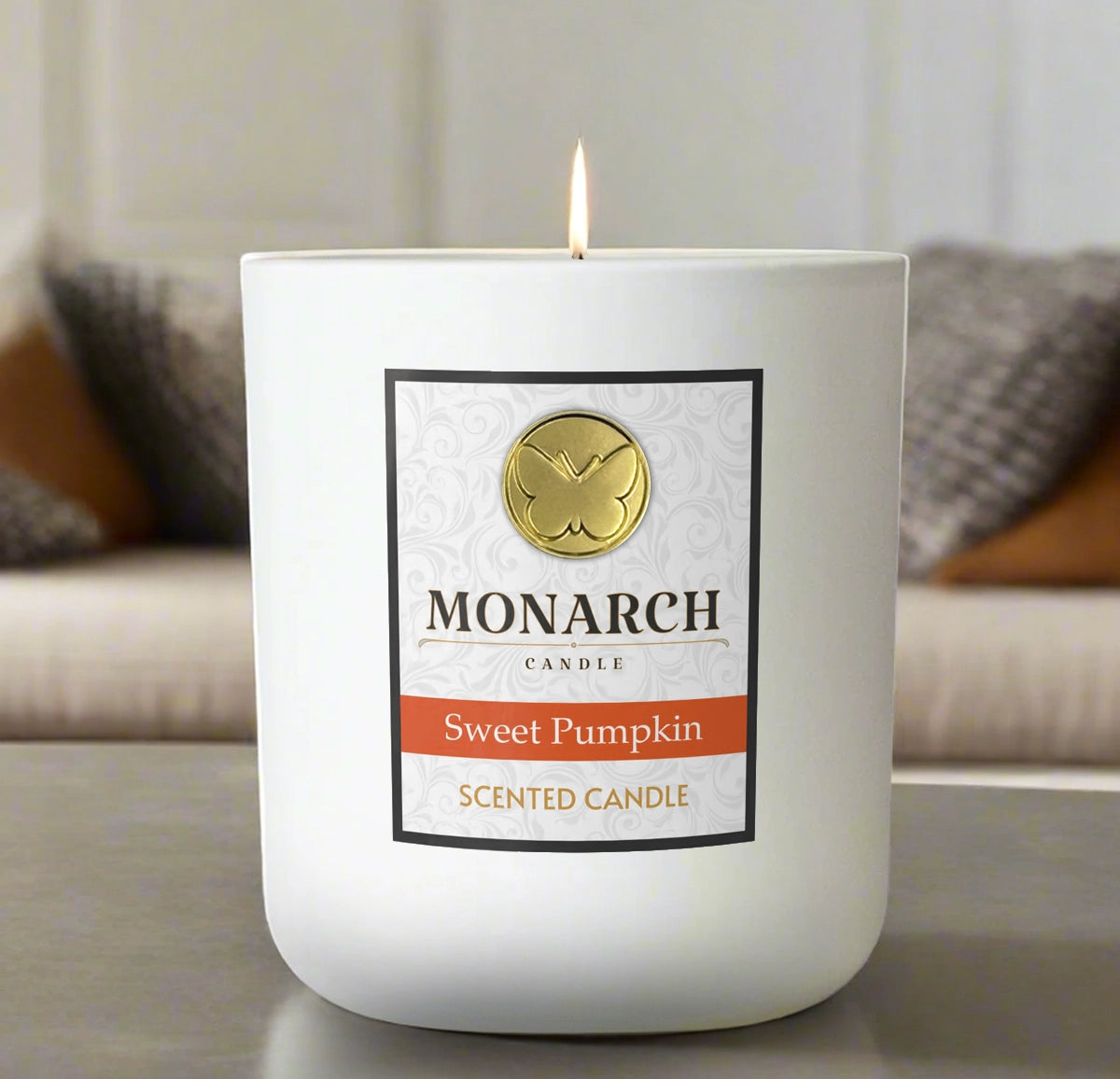 Monarch Candle labeled “Sweet Pumpkin” glowing gently in a white luxury glass vessel against a warm indoor background.