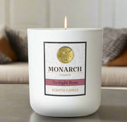 Monarch Candle labeled “Twilight Rose” glowing gently in a white luxury glass vessel against a warm indoor background.