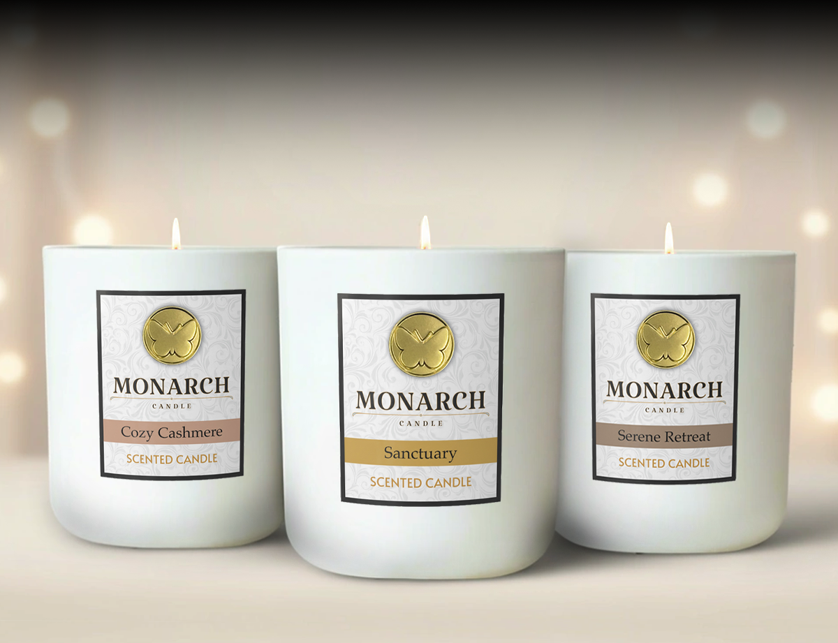 Three Monarch candles with labels on a blurred background. The candles are lit with labels that read "Cozy Cashmere", "Sanctuary", and "Serene Retreat".