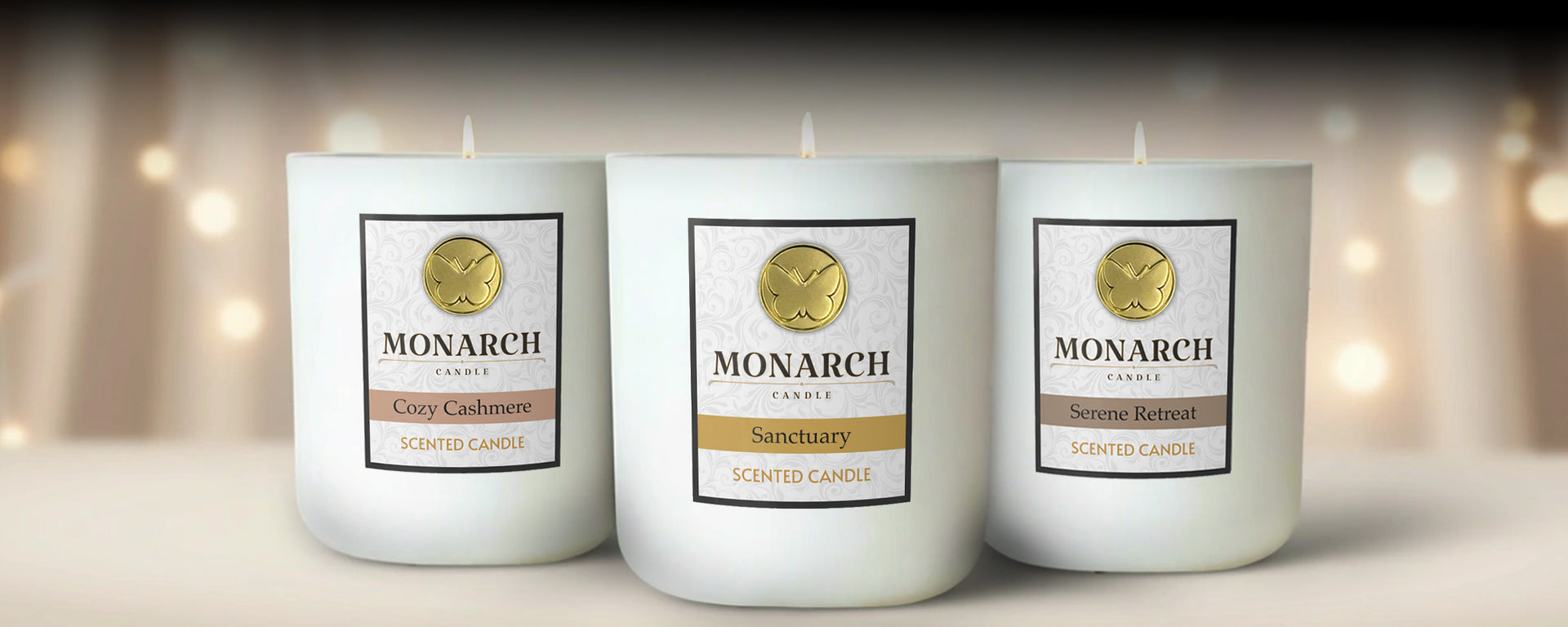 Three Monarch candles with labels on a blurred background. The candles are lit with labels that read "Cozy Cashmere", "Sanctuary", and "Serene Retreat".