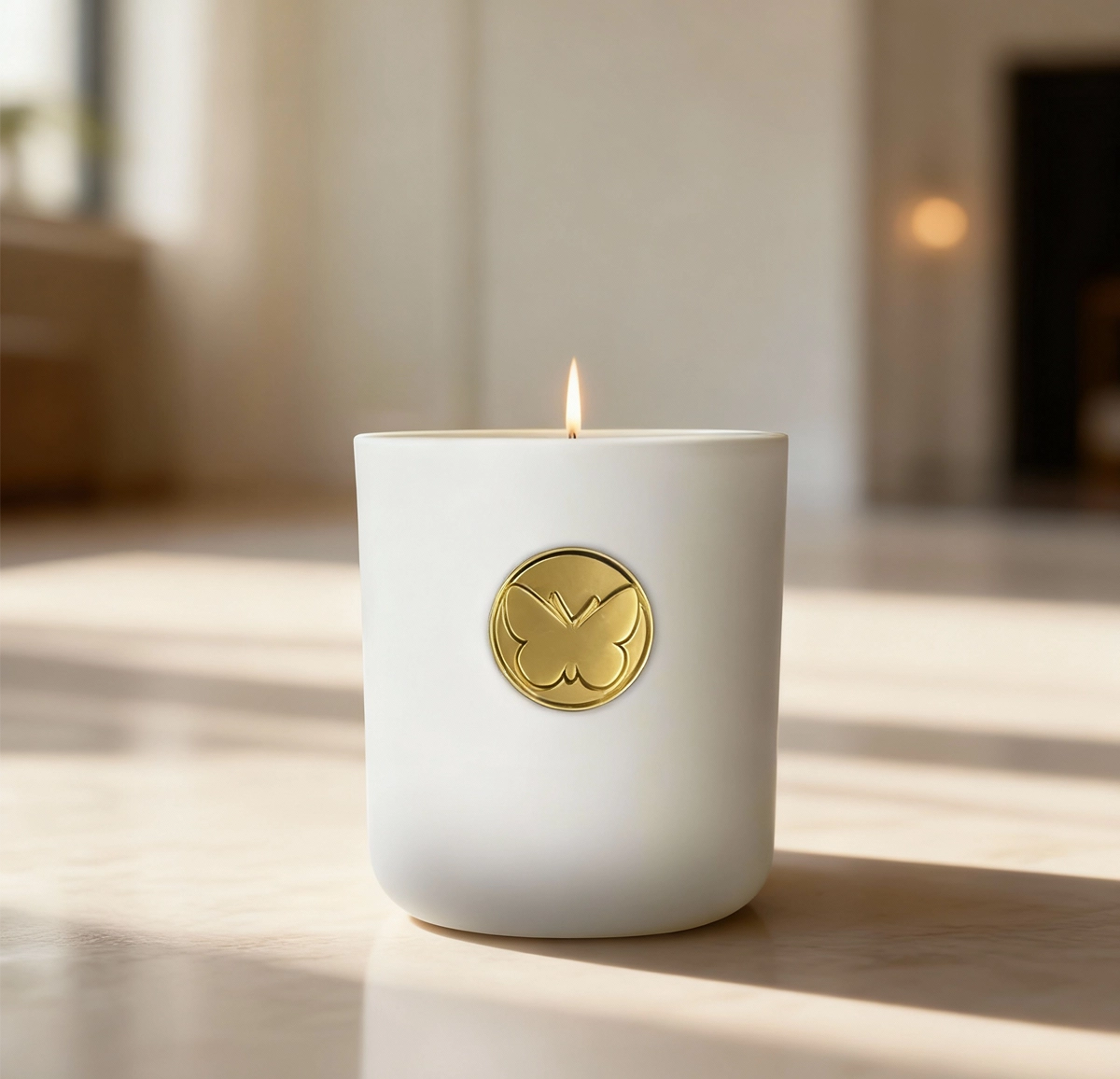 Monarch Candle votive glowing softly in a white luxury glass vessel with a gold butterfly charm on the front, placed on a table in a warm indoor setting.